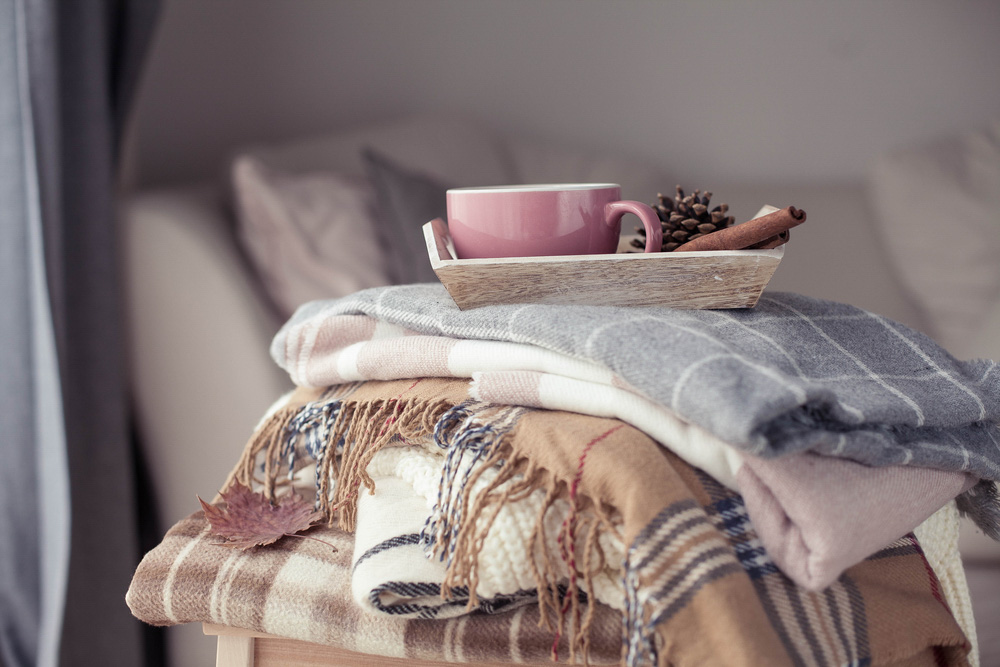 Beige arm chair with pile of blankets and a pink mug on top